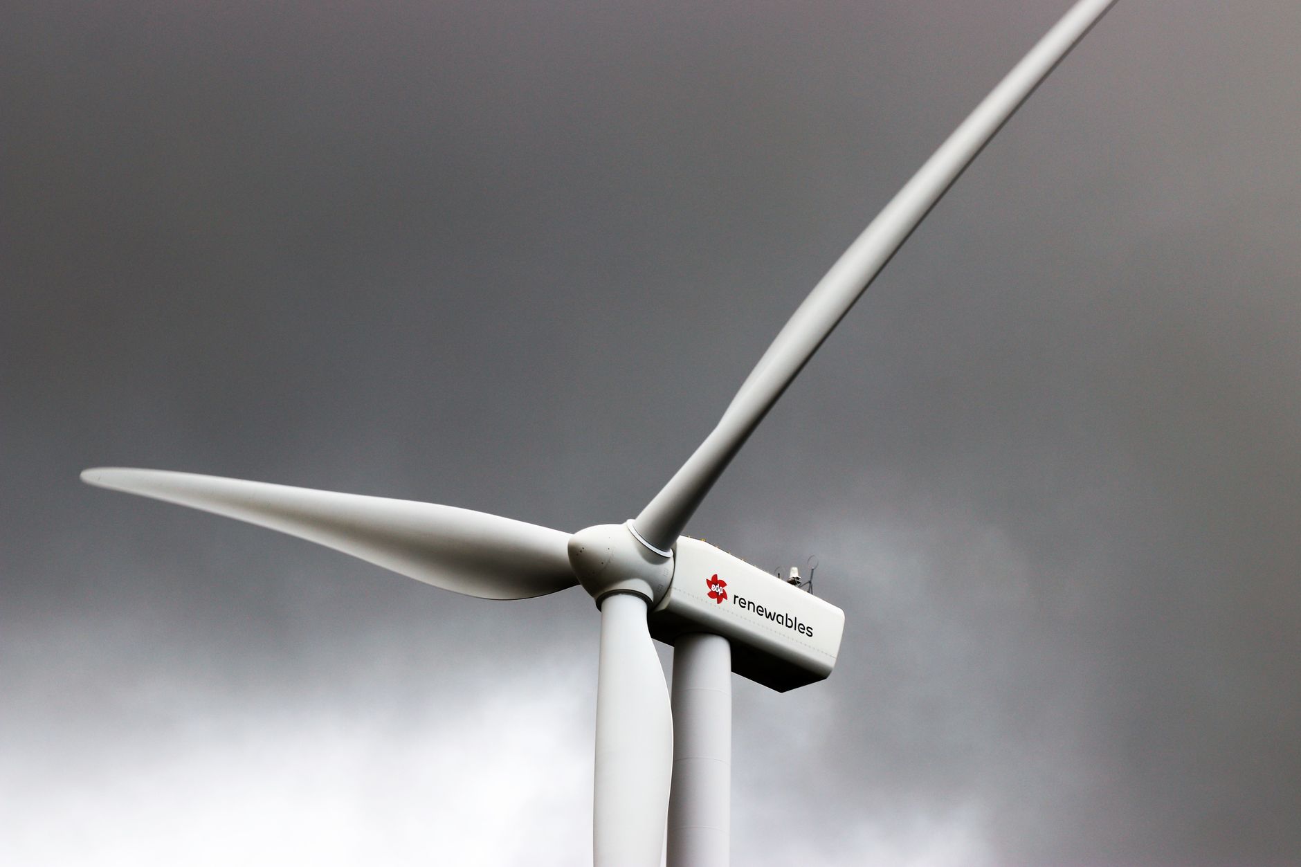 A wind turbine stands tall against dark, cloud-laden skies, symbolizing renewable energy.